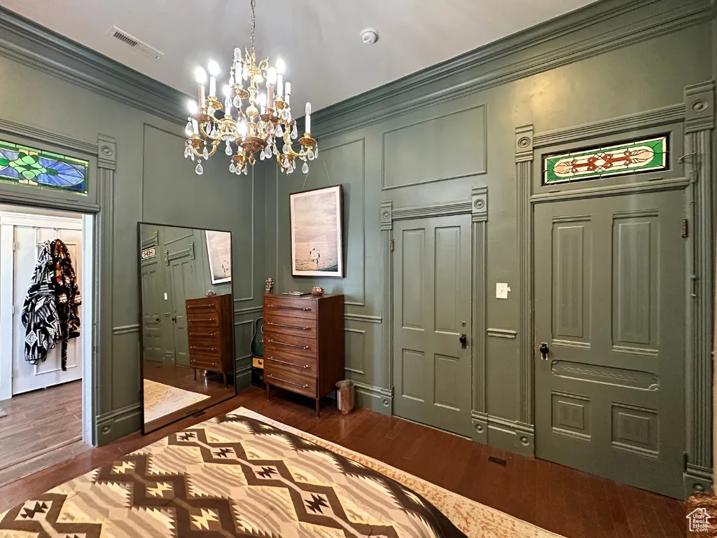 Bedroom with visible vents, dark wood-style flooring, crown molding, and a decorative wall