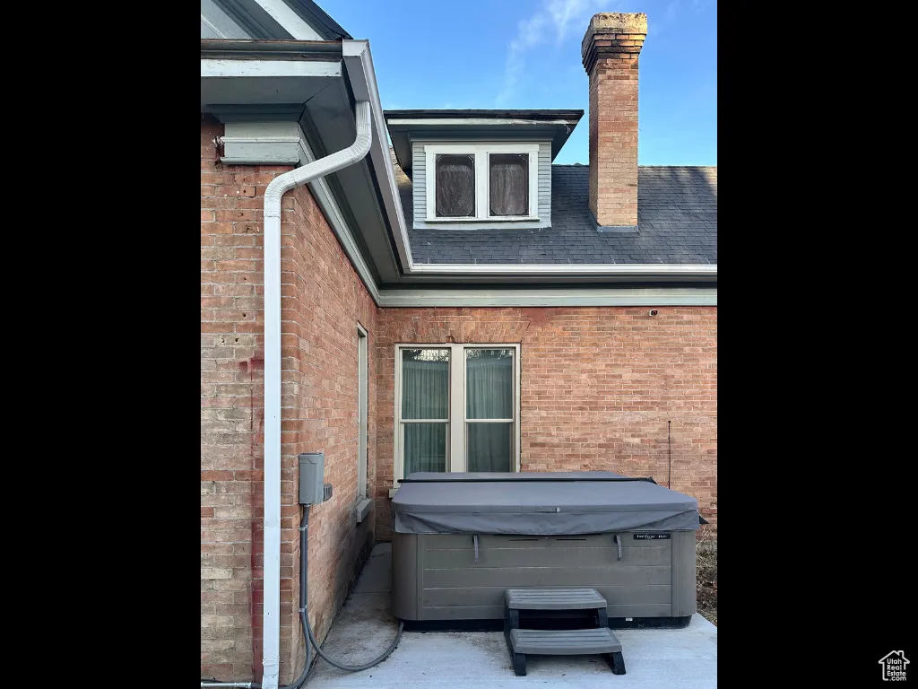 View of side of property featuring brick siding, a chimney, and a hot tub