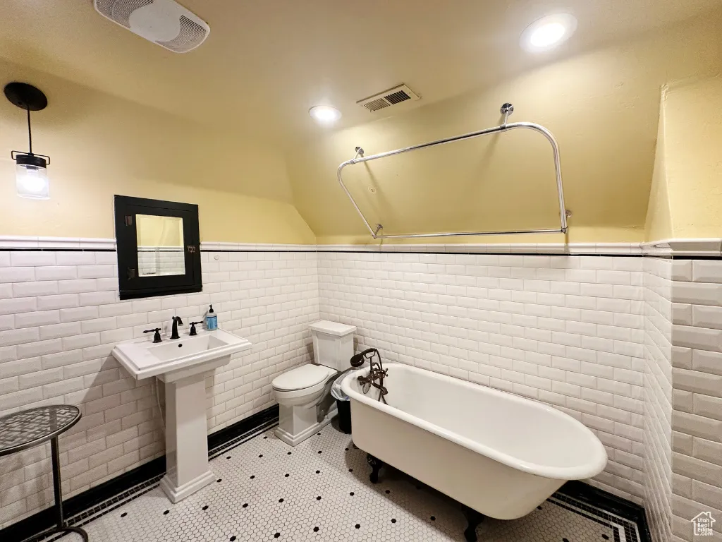 Full bathroom featuring visible vents, a wainscoted wall, toilet, lofted ceiling, and a freestanding tub