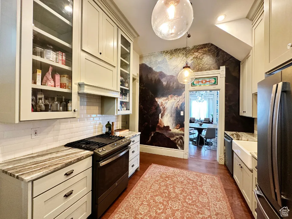 Kitchen featuring decorative light fixtures, dark wood-style floors, appliances with stainless steel finishes, glass insert cabinets, and light stone countertops