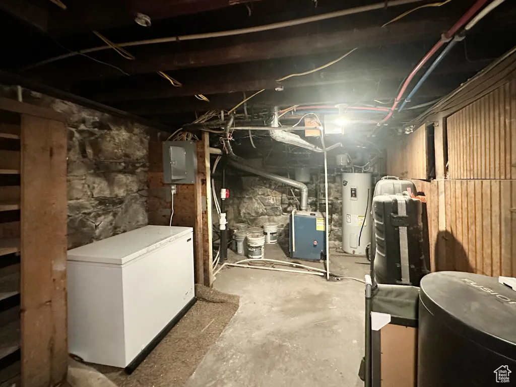 Unfinished basement with electric panel, refrigerator, and electric water heater