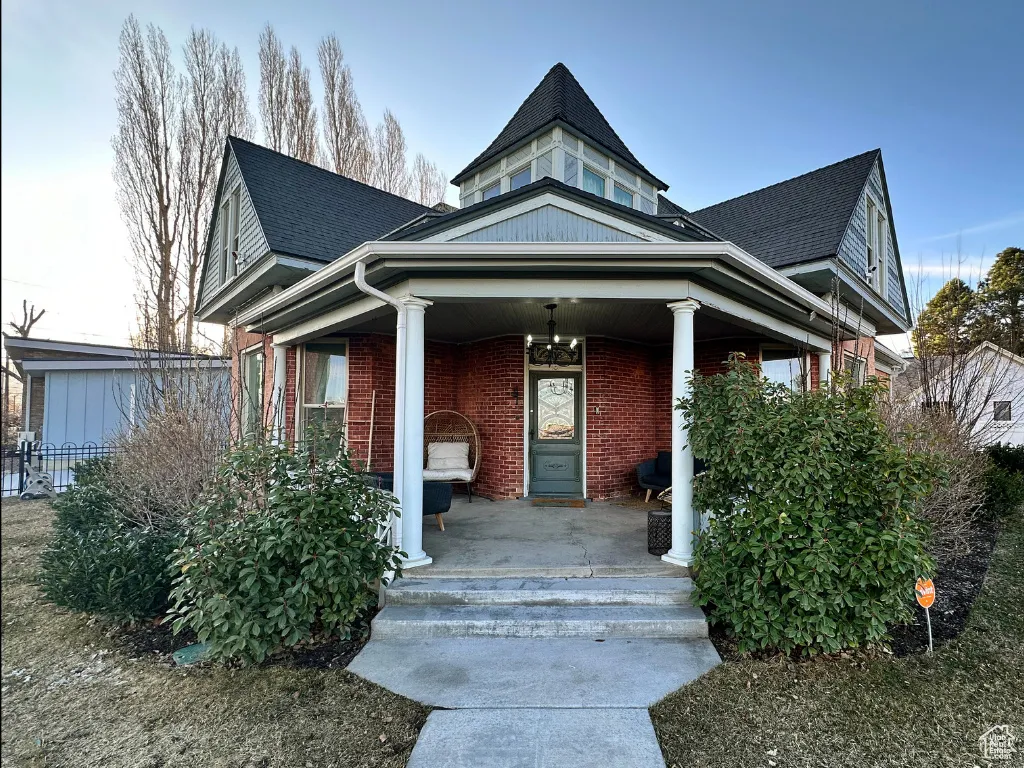 Victorian home featuring brick siding, a porch, and roof with shingles