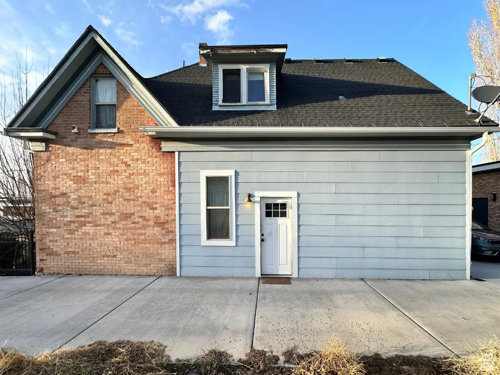 Back of property featuring a patio area, a shingled roof, and brick siding
