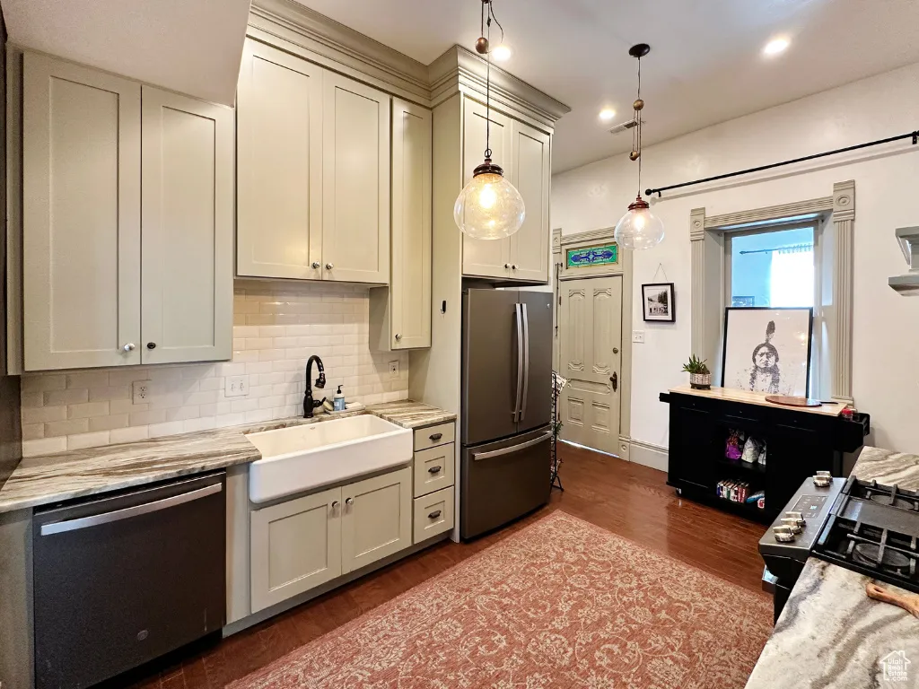 Kitchen featuring a sink, decorative light fixtures, tasteful backsplash, dark wood-style floors, and appliances with stainless steel finishes