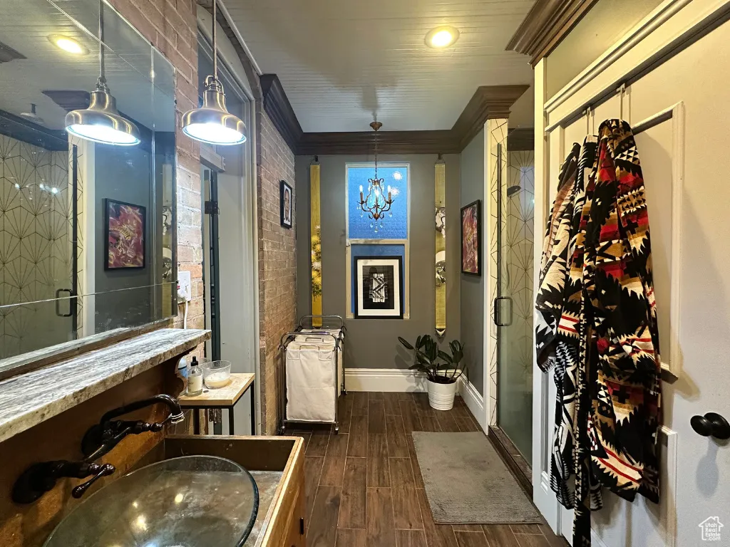 Bathroom with brick wall, baseboards, ornamental molding, a stall shower, and wood finished floors