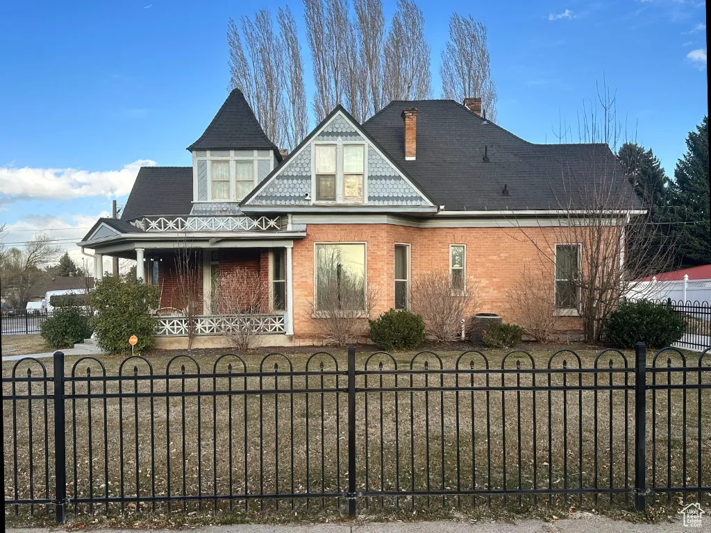 Victorian house with a fenced front yard, a porch, a chimney, and brick siding