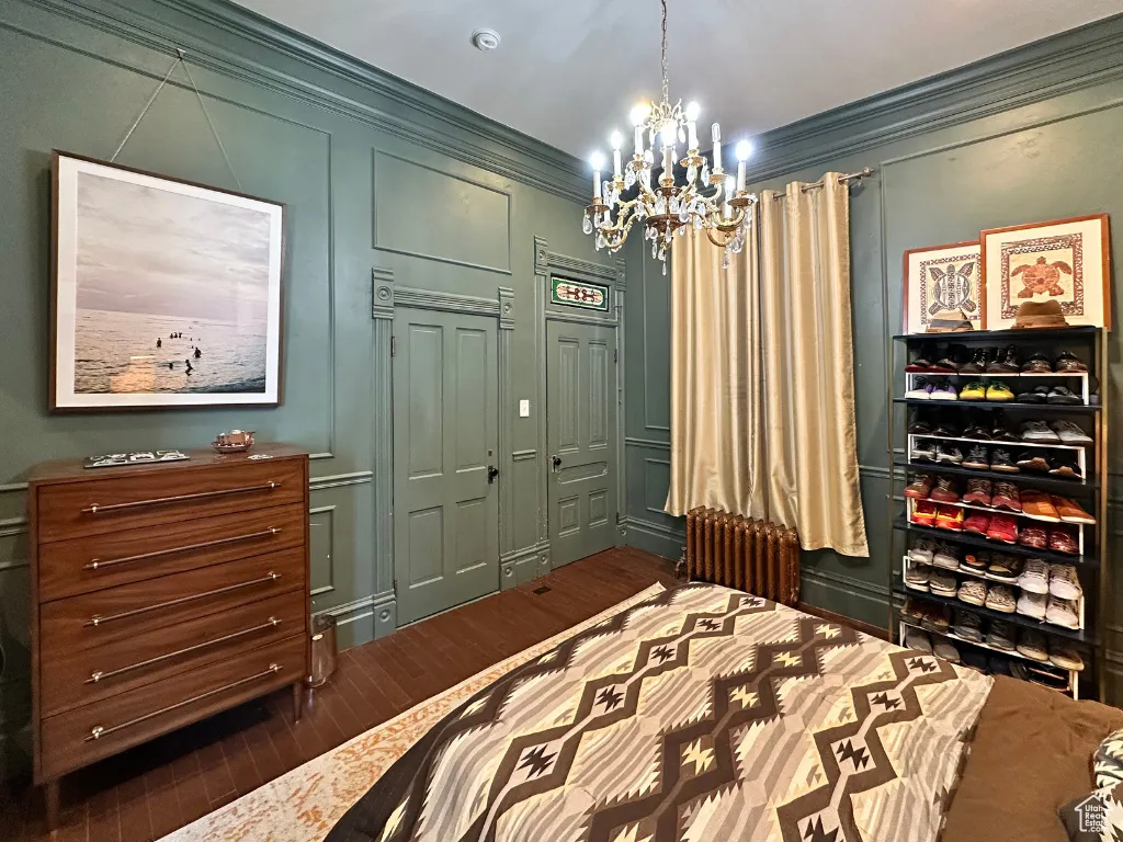 Bedroom with a notable chandelier, ornamental molding, dark wood finished floors, radiator, and a decorative wall