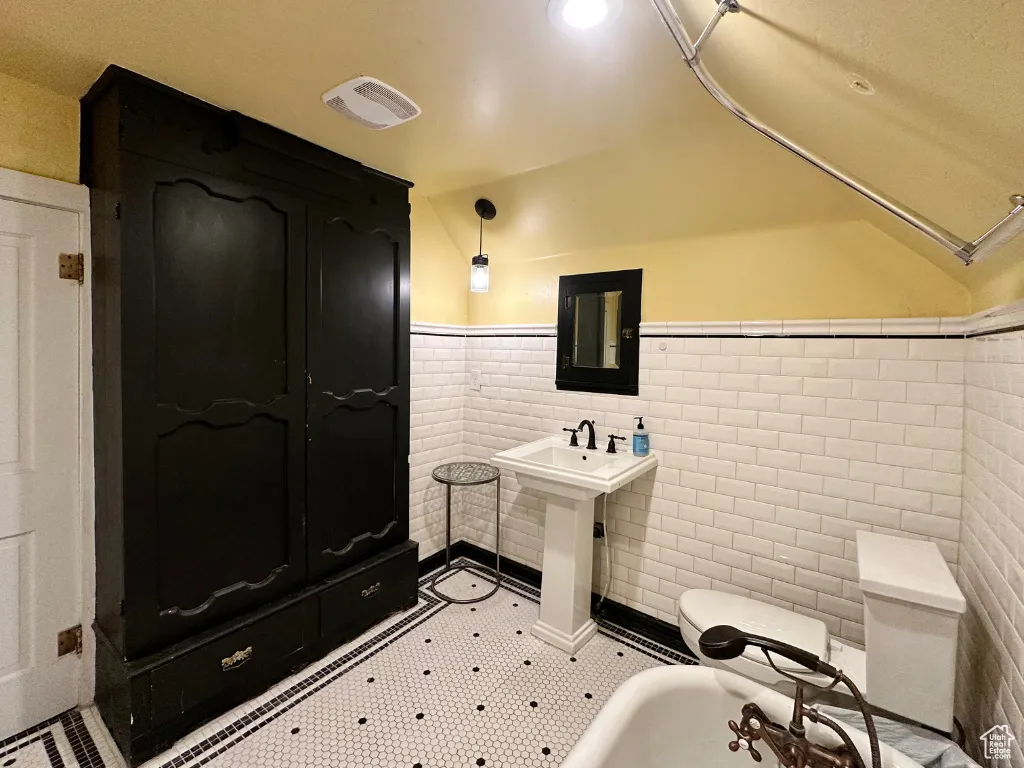 Bathroom featuring vaulted ceiling, visible vents, and a wainscoted wall
