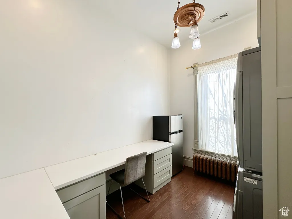 Home office with visible vents, stacked washer / dryer, radiator heating unit, built in desk, and dark wood-style floors
