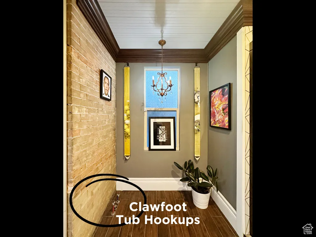 Interior space featuring baseboards, brick wall, wood tiled floor, an inviting chandelier, and ornamental molding
