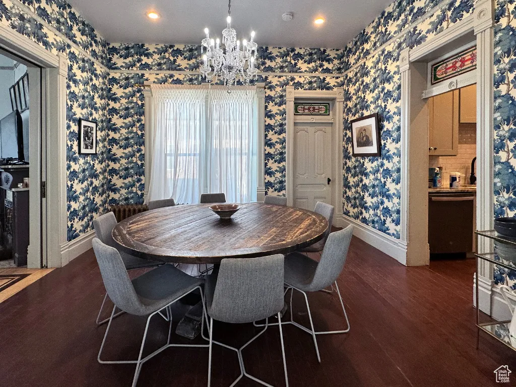 Dining room featuring dark wood finished floors, baseboards, wallpapered walls, and an inviting chandelier