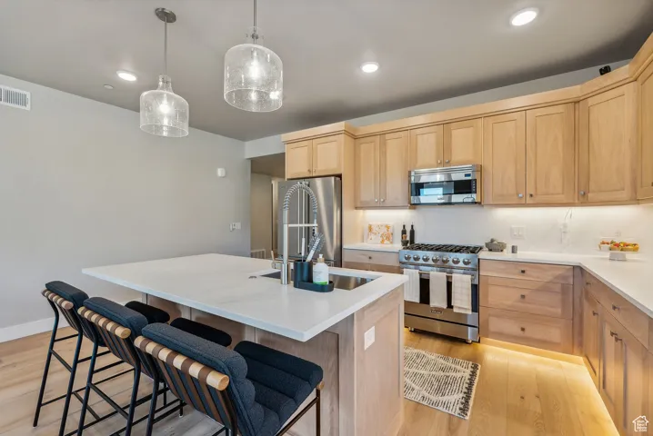 Kitchen with a breakfast bar, light brown cabinets, premium appliances, and light wood-type flooring