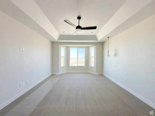 Unfurnished room with a tray ceiling, baseboards, ceiling fan, and a textured ceiling