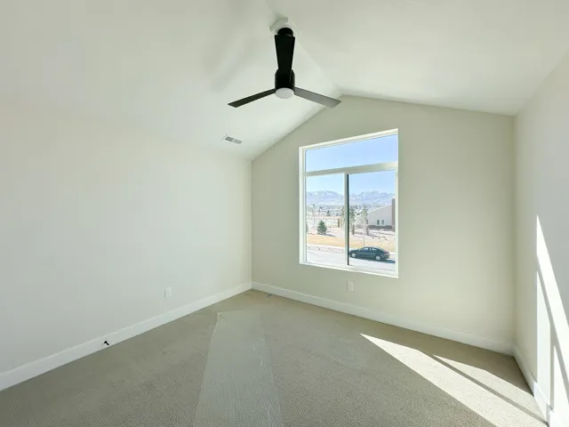 Spare room with visible vents, baseboards, ceiling fan, vaulted ceiling, and light colored carpet