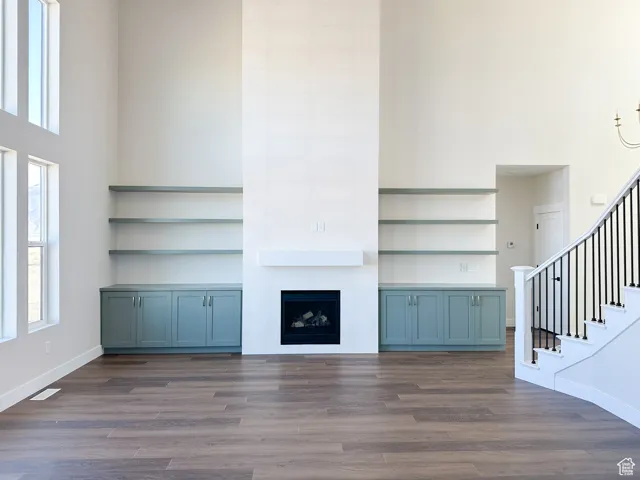 Unfurnished living room featuring stairs, wood finished floors, a towering ceiling, and baseboards