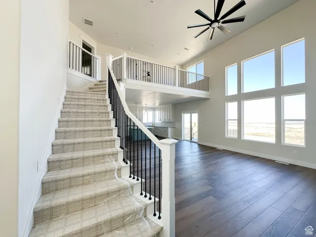 Staircase featuring baseboards, a towering ceiling, visible vents, a ceiling fan, and wood finished floors