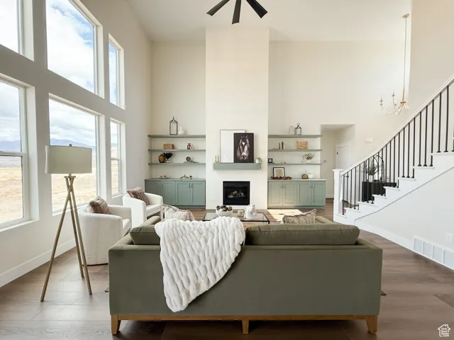 Living room featuring a tiled fireplace, a towering ceiling, wood finished floors, and stairs