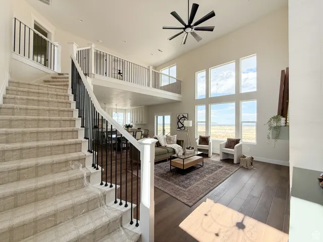 Living room with dark wood-style floors, a high ceiling, stairs, a ceiling fan, and a water view
