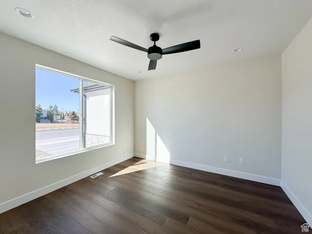 Unfurnished room featuring dark wood-type flooring, baseboards, a textured ceiling, visible vents, and a ceiling fan
