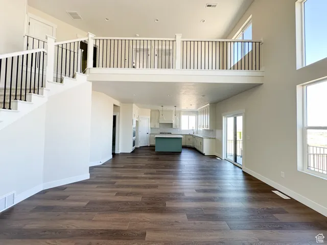 Unfurnished living room featuring baseboards, visible vents, a high ceiling, and dark wood-type flooring