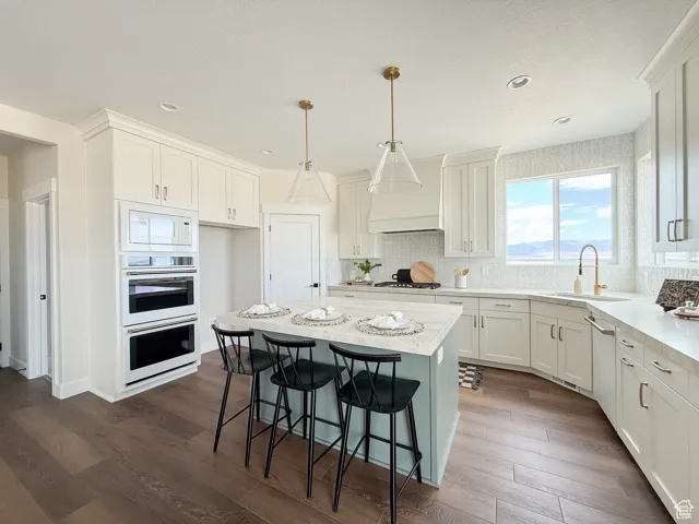 Kitchen featuring a kitchen bar, a kitchen island, hanging light fixtures, white cabinetry, and dark wood-style flooring