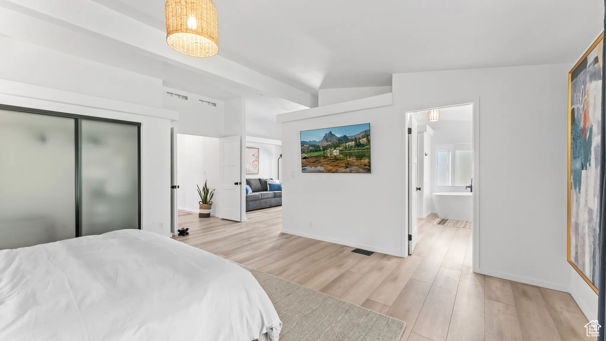 Bedroom with vaulted ceiling, light wood-style floors, baseboards, and connected bathroom
