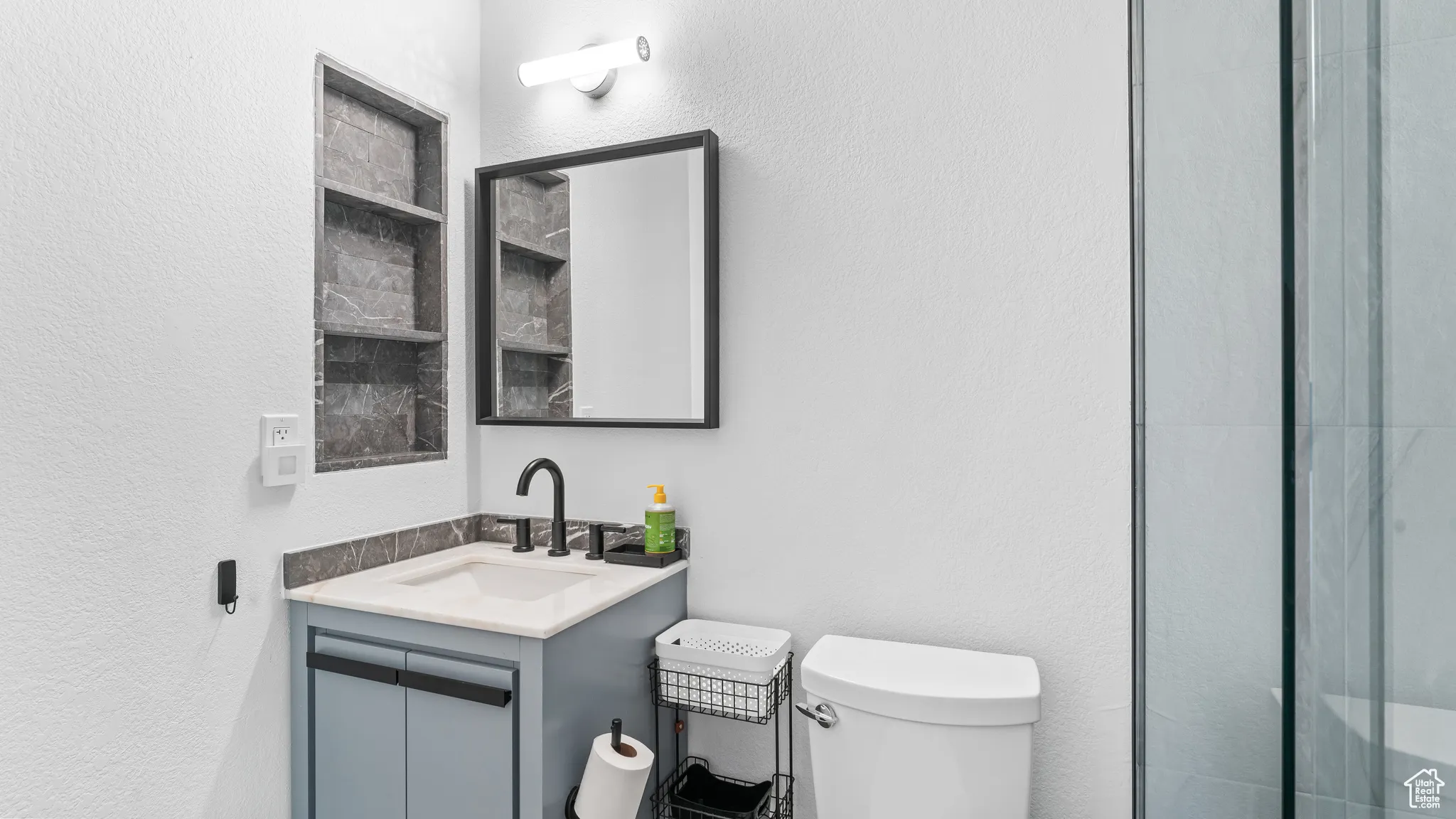 Bathroom with toilet, vanity, and a textured wall