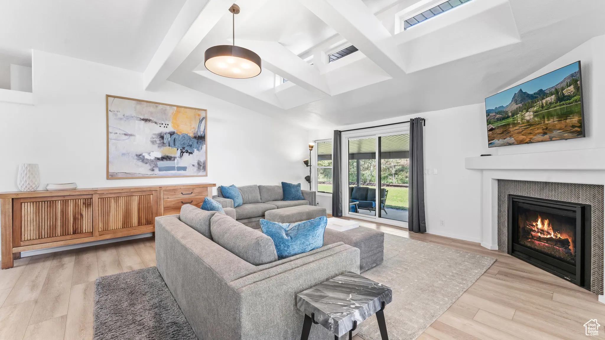 Living area with light wood-style flooring, a glass covered fireplace, and vaulted ceiling with beams