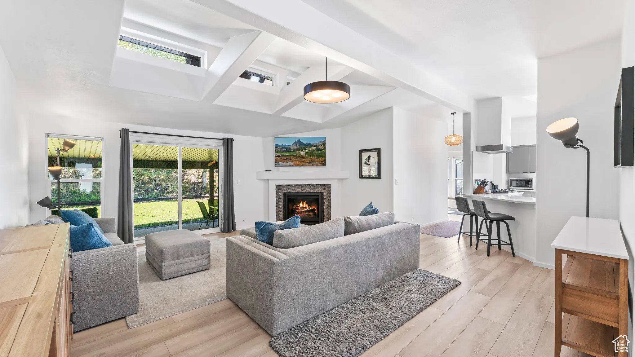 Living area featuring baseboards, coffered ceiling, light wood finished floors, a glass covered fireplace, and beamed ceiling