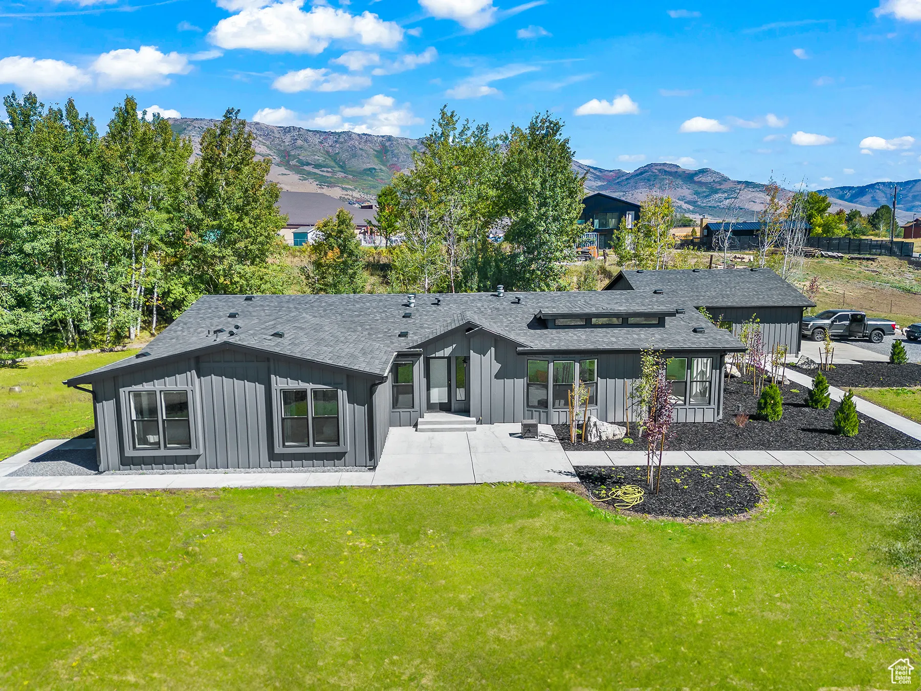 Rear view of house featuring board and batten siding, a shingled roof, a yard, a patio area, and a mountain view