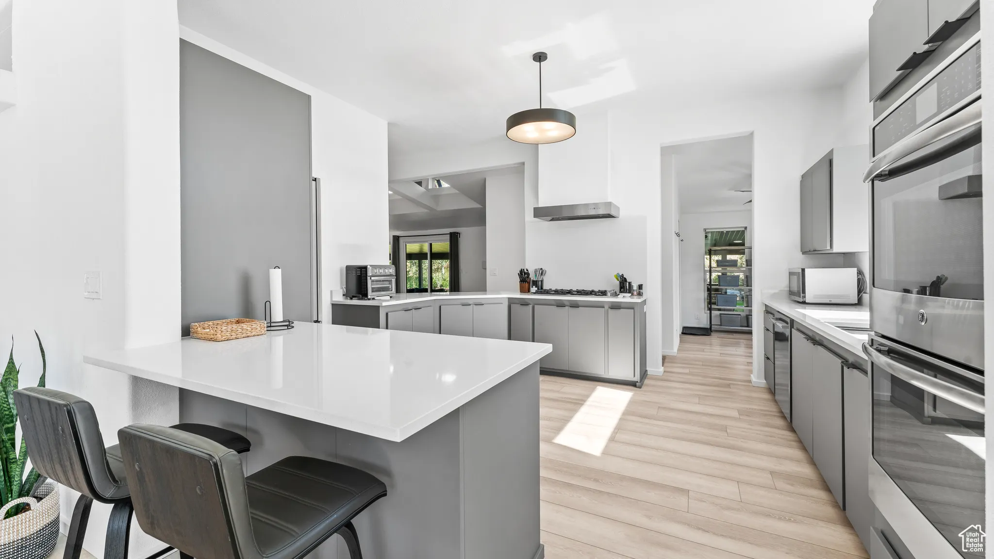 Kitchen featuring a kitchen bar, gray cabinetry, light wood-style floors, a peninsula, and appliances with stainless steel finishes