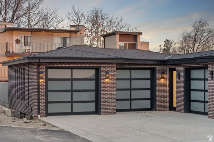 View of front of property featuring brick siding, driveway, a garage, and roof with shingles