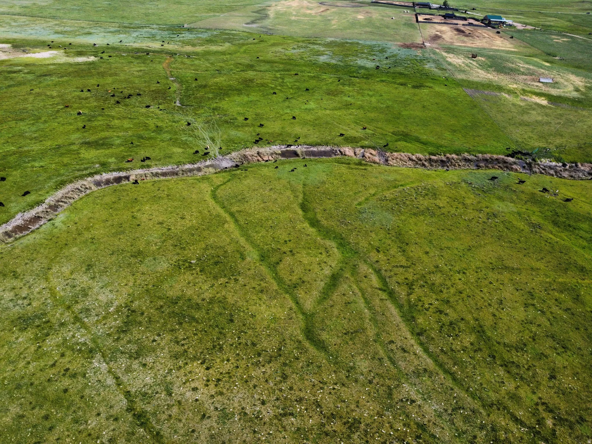 Expansive green pastures featuring a winding creek bed, multiple buildings, and open land
