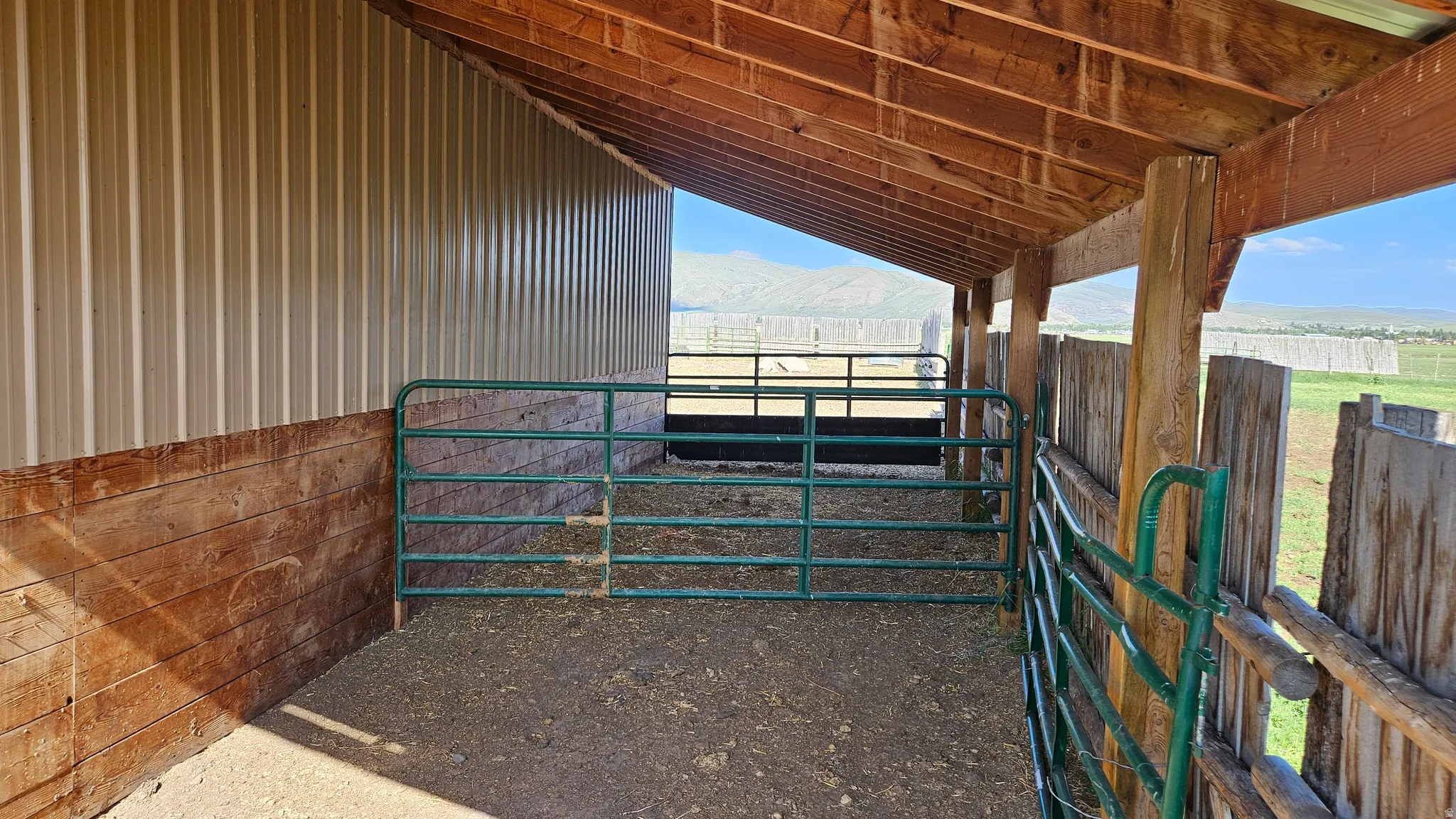 Covered animal enclosure featuring a wood-beam ceiling, corrugated metal siding, and a wood plank kickboard