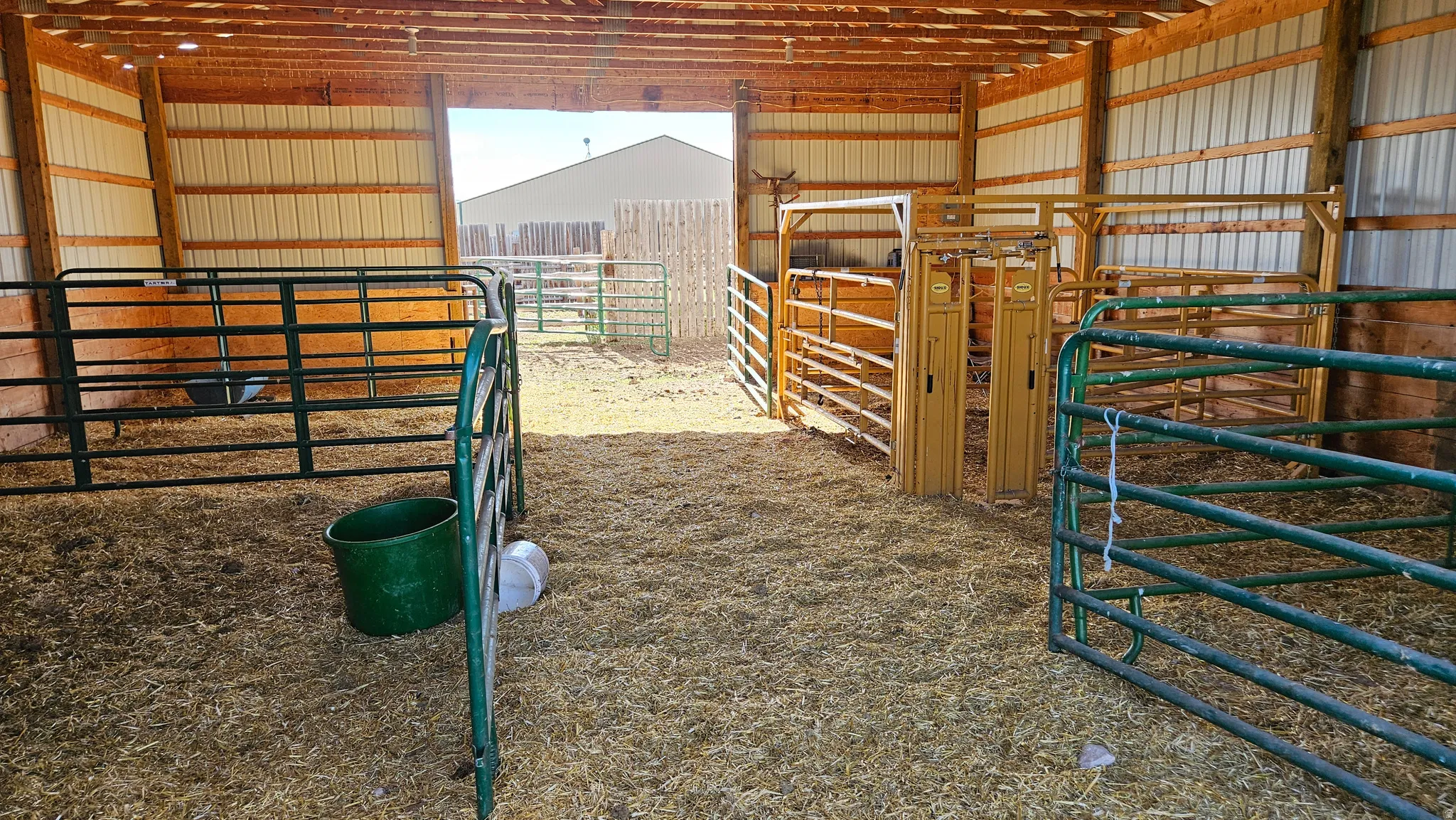 Barn interior featuring exposed wood beams, corrugated metal walls, and a dirt floor with straw