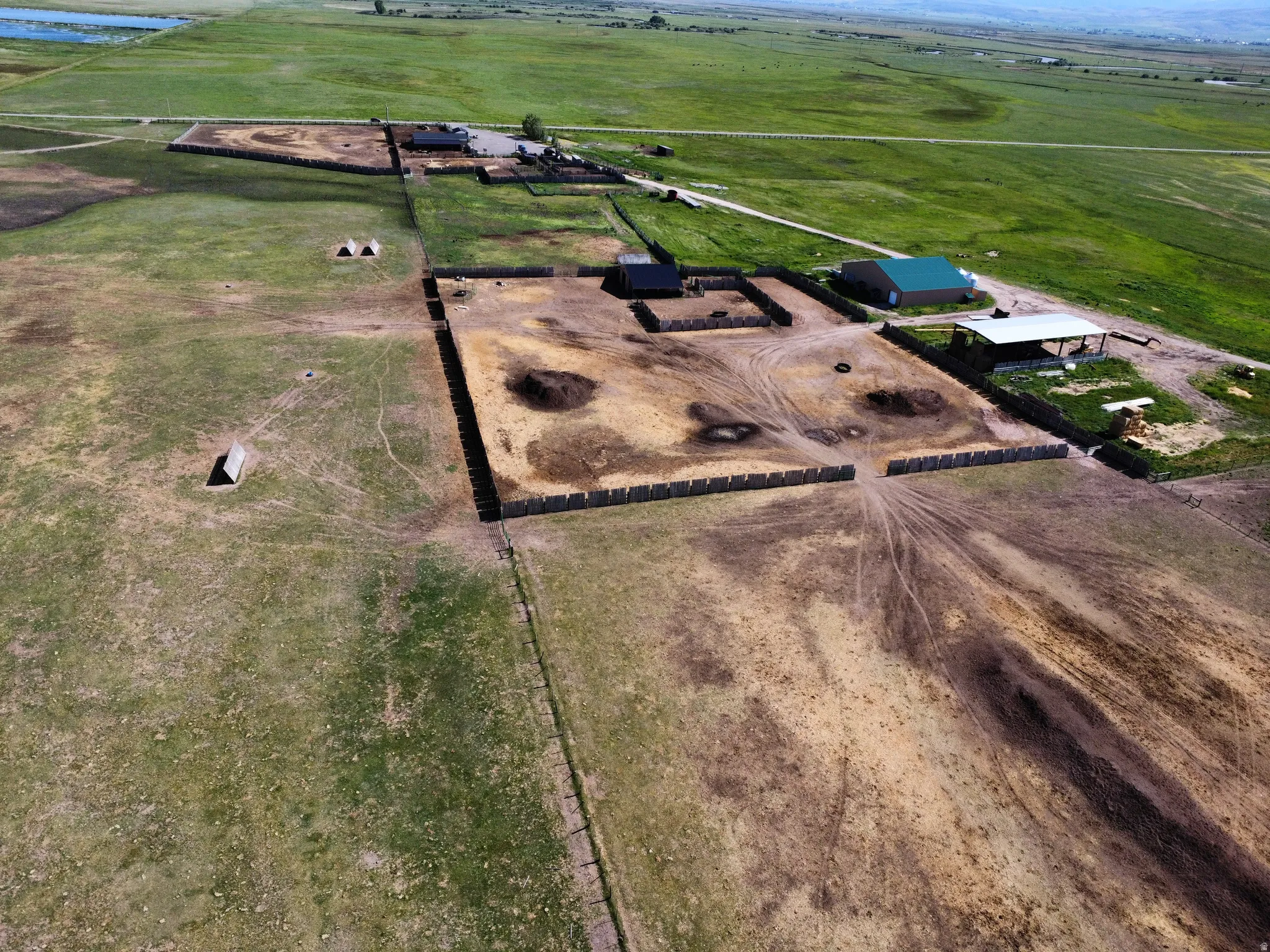 Extensive agricultural property featuring multiple fenced enclosures, a large barn with a green roof, a covered open-air structure, and substantial acreage