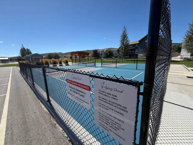 Fenced pickleball court with a blue surface, white court lines, and an adjacent wood pergola