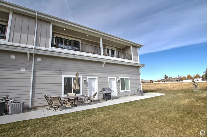 Back of property featuring a balcony, a yard, central AC, a patio area, and board and batten siding
