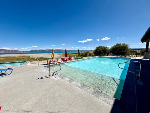 Outdoor swimming pool with integrated hot tub, concrete pool deck, and metal handrails