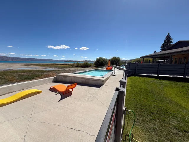 Concrete patio with a built-in hot tub, bordering a body of water, and a fenced lawn area