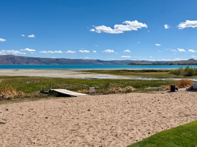 Expansive sandy beach area with a wooden ramp leading to the water, bordered by natural vegetation
