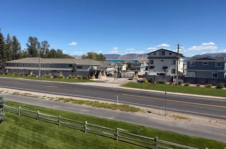 Gated community entrance with stone accents, manicured green space, and distant water scenery