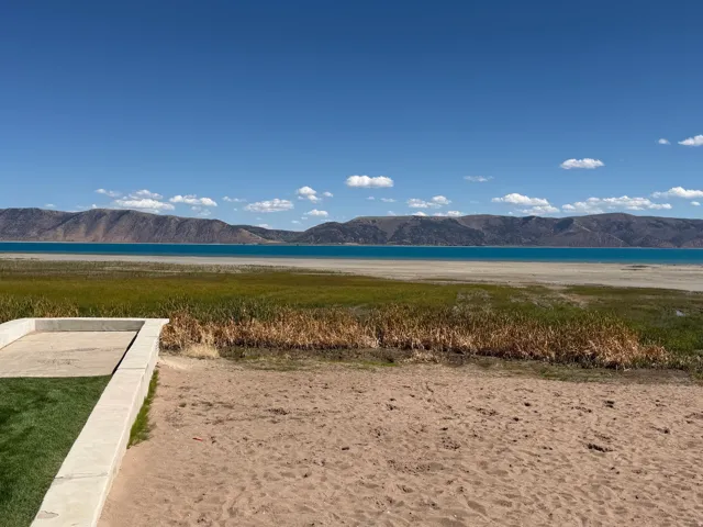 Lakeside property featuring a concrete-edged lawn area, sandy terrain, and vibrant blue waters