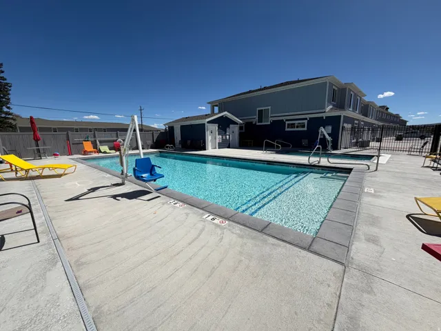 Outdoor swimming pool with concrete decking, perimeter fencing, and a building featuring blue siding