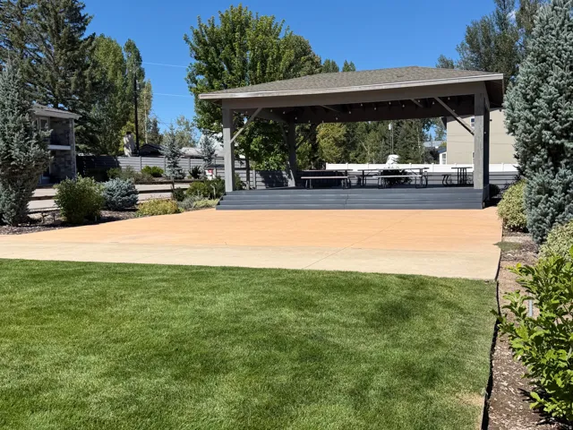Expansive green lawn with a concrete patio, featuring a covered pergola and established landscaping