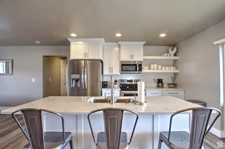 Kitchen featuring a center island with sink, backsplash, dark wood finished floors, white cabinetry, and stainless steel appliances