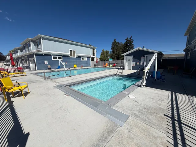 Two swimming pools with concrete surrounds, a dark blue exterior pool house, and a perimeter fence