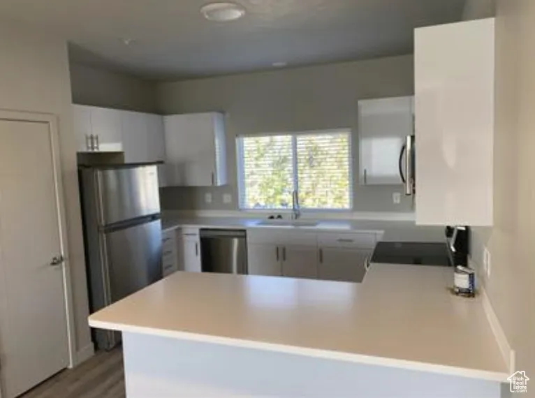 Kitchen featuring light countertops, light wood-type flooring, a sink, a peninsula, and appliances with stainless steel finishes