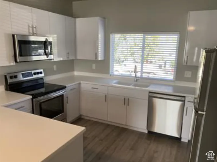 Kitchen featuring light countertops, dark wood-style flooring, a sink, white cabinets, and appliances with stainless steel finishes
