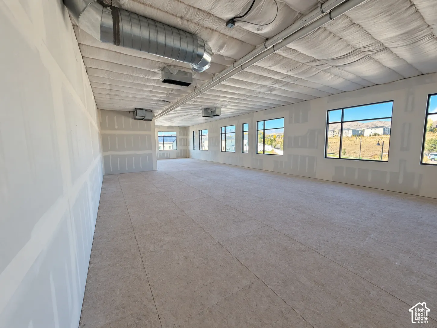 Expansive open-concept interior featuring high ceilings with exposed ductwork, large multi-pane windows, and neutral-finish flooring